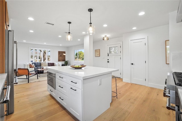 kitchen featuring recessed lighting, visible vents, light wood-style floors, white cabinets, and a kitchen bar