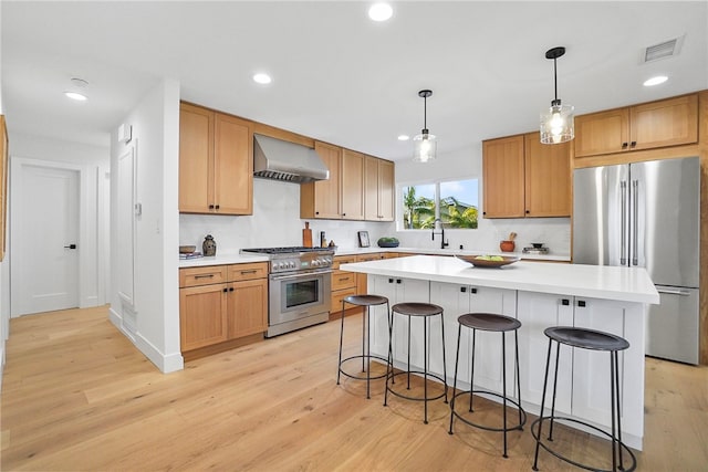 kitchen featuring appliances with stainless steel finishes, a breakfast bar, light countertops, and wall chimney range hood