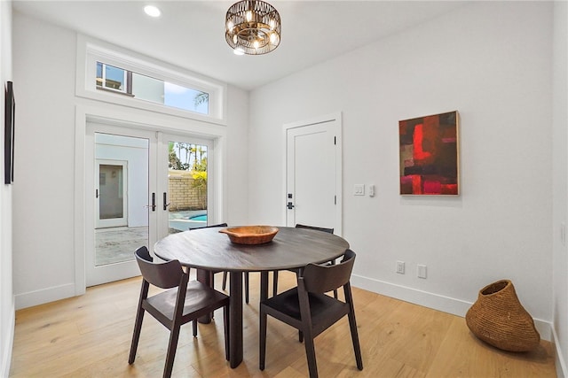 dining area featuring light wood-type flooring, french doors, a notable chandelier, and baseboards