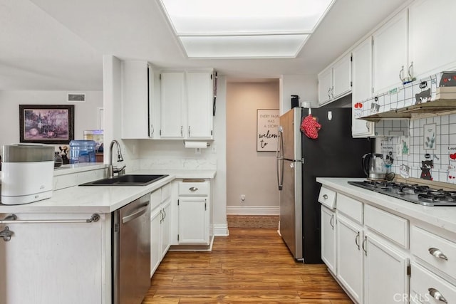 kitchen featuring white cabinetry, stainless steel appliances, light hardwood / wood-style floors, sink, and backsplash