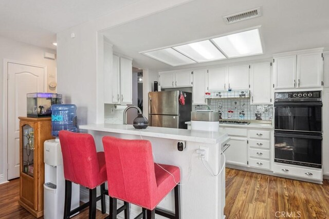 kitchen featuring kitchen peninsula, appliances with stainless steel finishes, white cabinets, and a breakfast bar