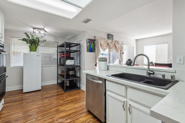 kitchen featuring dishwasher, hardwood / wood-style floors, sink, white cabinetry, and light stone counters