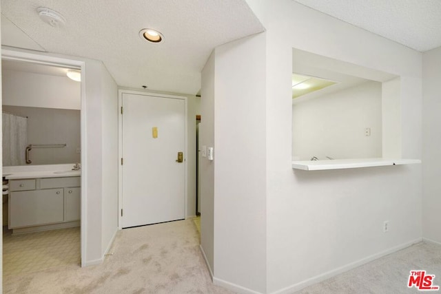 hall featuring a textured ceiling, light colored carpet, and sink