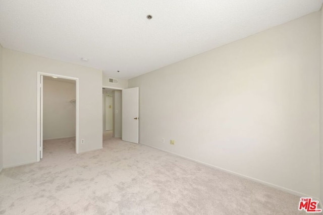 unfurnished bedroom featuring a walk in closet, light carpet, and a closet