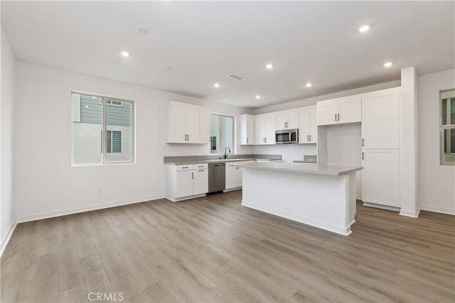 kitchen featuring appliances with stainless steel finishes, white cabinets, a center island, light hardwood / wood-style floors, and a healthy amount of sunlight