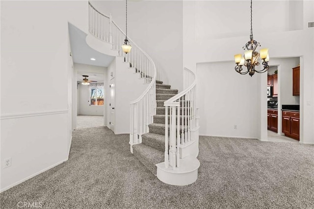 stairway featuring carpet flooring, a high ceiling, and ceiling fan with notable chandelier