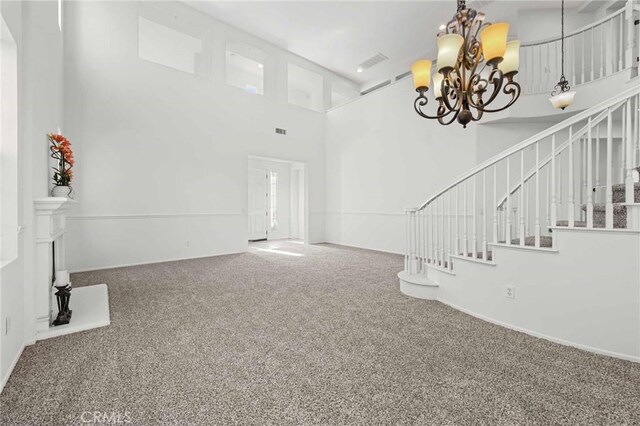 unfurnished living room with carpet flooring, a towering ceiling, and an inviting chandelier