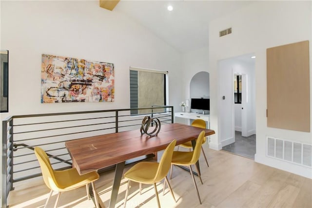 dining space with high vaulted ceiling and light hardwood / wood-style flooring