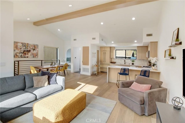 living room featuring beam ceiling, sink, high vaulted ceiling, and light hardwood / wood-style floors