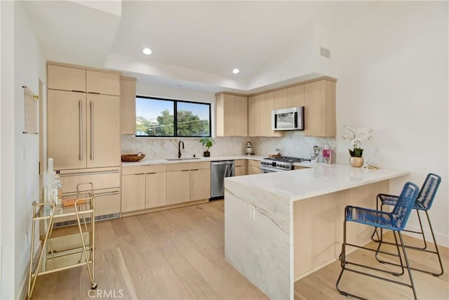 kitchen featuring kitchen peninsula, light brown cabinetry, light wood-type flooring, stainless steel appliances, and sink