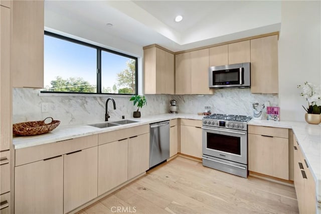 kitchen with sink, stainless steel appliances, backsplash, light brown cabinetry, and light wood-type flooring