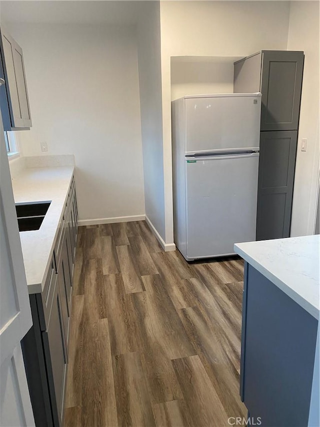 kitchen featuring dark wood-type flooring, white refrigerator, sink, light stone counters, and gray cabinetry