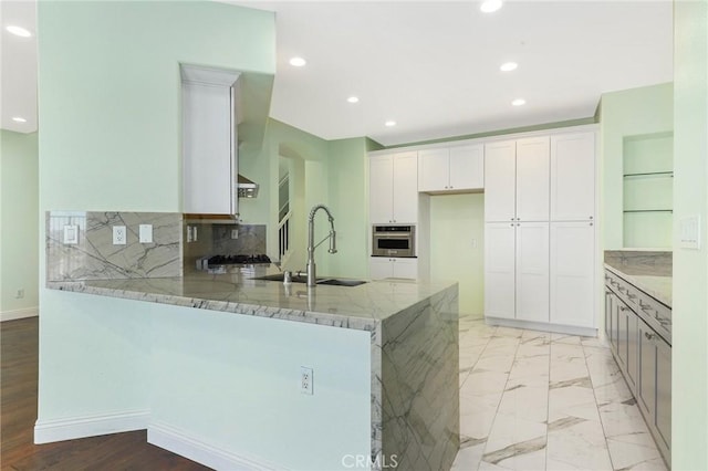 kitchen featuring sink, white cabinetry, stainless steel oven, light stone countertops, and decorative backsplash