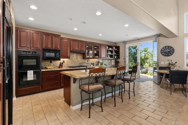 kitchen with a breakfast bar, glass insert cabinets, a kitchen island with sink, light stone countertops, and black appliances