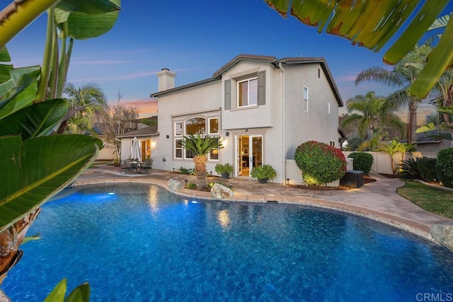 back of house at dusk with a patio, an outdoor pool, fence, and stucco siding