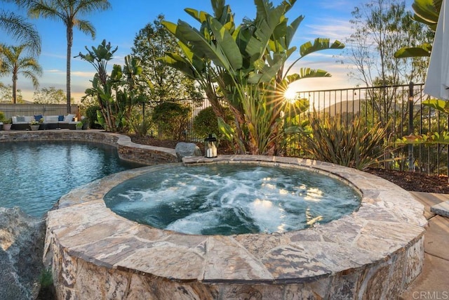 pool at dusk featuring a fenced in pool, fence, and an in ground hot tub