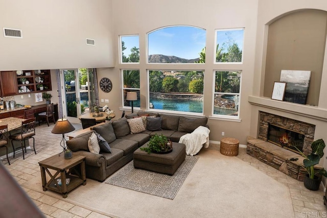 living area with visible vents, a stone fireplace, and a high ceiling