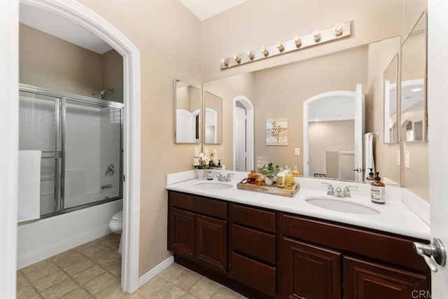 bathroom with enclosed tub / shower combo, double vanity, a sink, and toilet