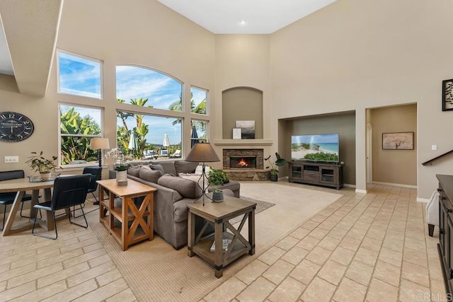 living room featuring a stone fireplace, brick floor, a towering ceiling, and baseboards