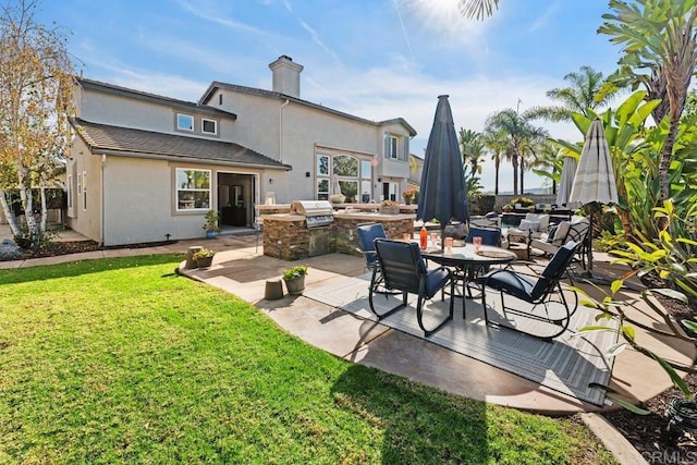 rear view of house featuring a yard, a chimney, a patio, stucco siding, and an outdoor kitchen