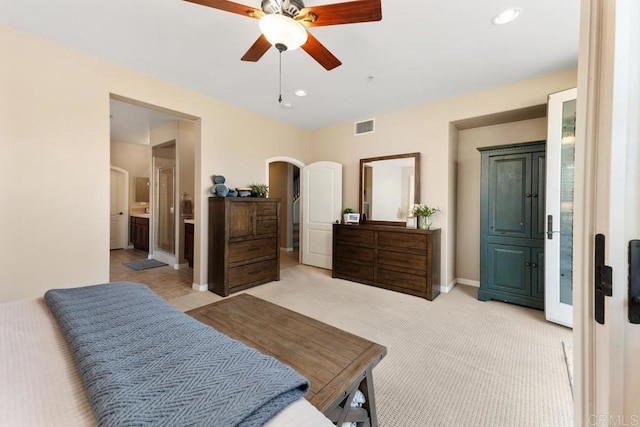 bedroom with arched walkways, light colored carpet, visible vents, baseboards, and ensuite bath