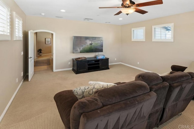 living area with baseboards, arched walkways, ceiling fan, and light colored carpet