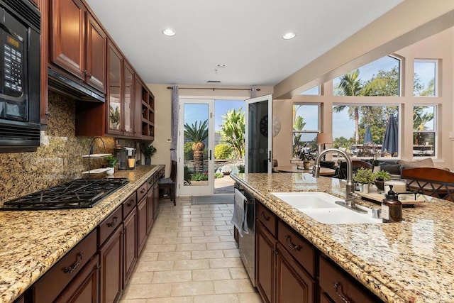 kitchen with black microwave, gas stovetop, a sink, decorative backsplash, and glass insert cabinets