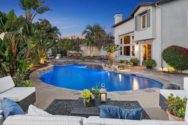 pool at dusk with outdoor lounge area, a patio area, and an outdoor pool