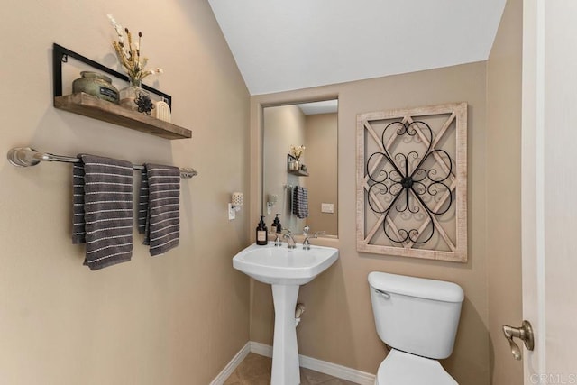 half bath with lofted ceiling, toilet, and baseboards