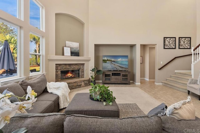 living area featuring light tile patterned floors, a stone fireplace, a towering ceiling, baseboards, and stairway