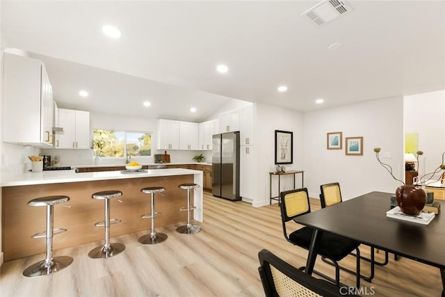 kitchen with stainless steel fridge, a kitchen bar, white cabinetry, and kitchen peninsula