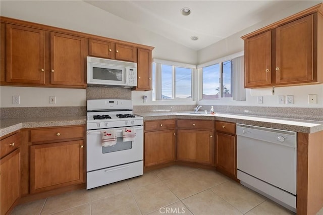 9551 San Rafael Dr, Desert Hot Springs, CA 92240 - kitchen with white appliances, lofted ceiling, brown cabinetry, light tile patterned floors, and light countertops