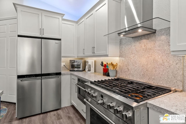 kitchen featuring white cabinets, vaulted ceiling, wall chimney exhaust hood, wood-type flooring, and stainless steel appliances