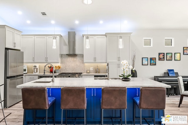 kitchen featuring appliances with stainless steel finishes, a kitchen island with sink, wall chimney exhaust hood, and sink