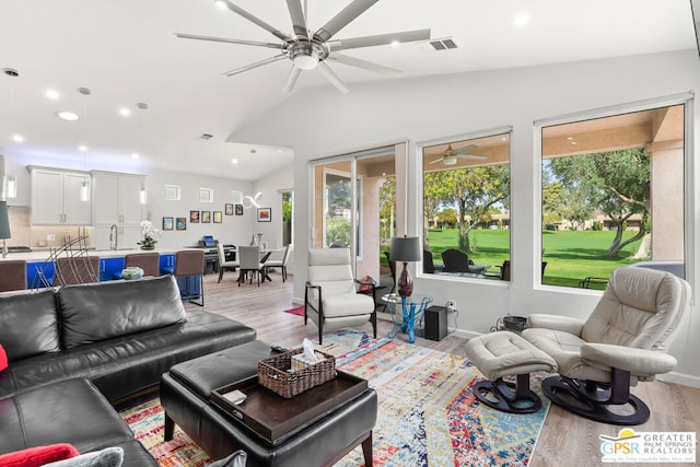 living room featuring a wealth of natural light, light hardwood / wood-style flooring, lofted ceiling, and sink