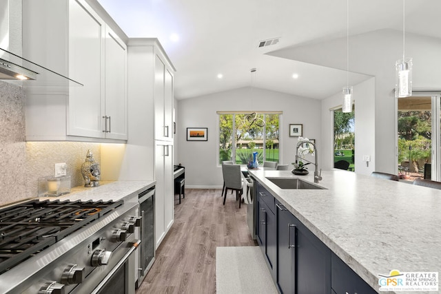 kitchen featuring white cabinetry, sink, wall chimney range hood, light hardwood / wood-style floors, and decorative light fixtures