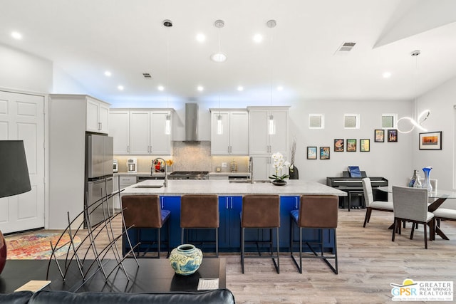 kitchen featuring wall chimney exhaust hood, sink, pendant lighting, light hardwood / wood-style flooring, and white cabinetry