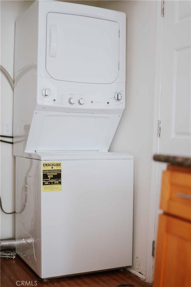 clothes washing area with dark hardwood / wood-style flooring and stacked washer / drying machine