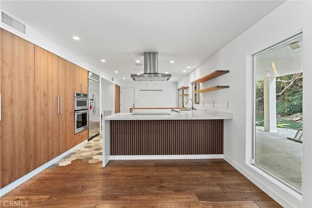 kitchen featuring sink, dark hardwood / wood-style floors, double oven, kitchen peninsula, and island exhaust hood