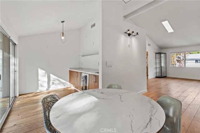 dining space featuring high vaulted ceiling, a skylight, and light hardwood / wood-style flooring