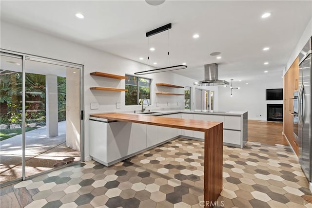 kitchen featuring butcher block counters, white cabinets, pendant lighting, and wall chimney range hood