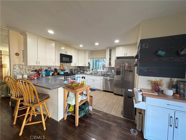 kitchen featuring kitchen peninsula, stainless steel appliances, sink, dark hardwood / wood-style floors, and white cabinetry