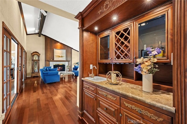 bar featuring a sink, vaulted ceiling with beams, a warm lit fireplace, wet bar, and dark wood-style flooring