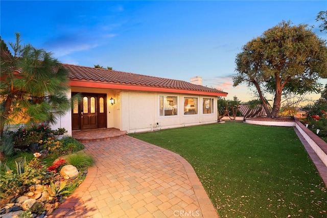 view of front of property featuring stucco siding, a tiled roof, a chimney, and a front yard