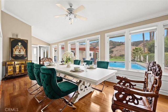 dining area with visible vents, a ceiling fan, wood finished floors, crown molding, and vaulted ceiling