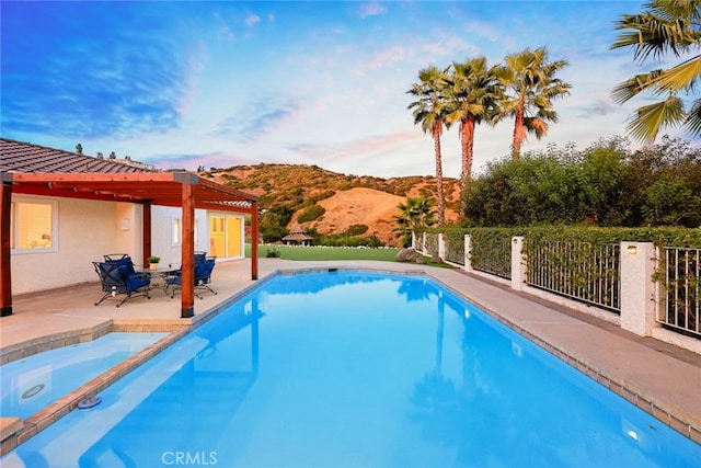 view of swimming pool featuring a pool with connected hot tub, fence, a patio area, a mountain view, and a pergola