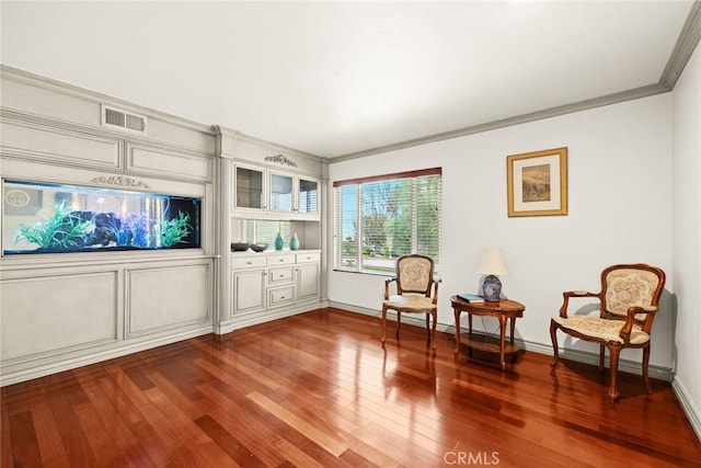 living area featuring crown molding, wood finished floors, visible vents, and baseboards