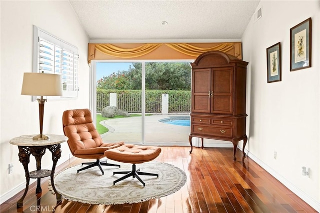 living area featuring visible vents, a textured ceiling, wood finished floors, baseboards, and lofted ceiling