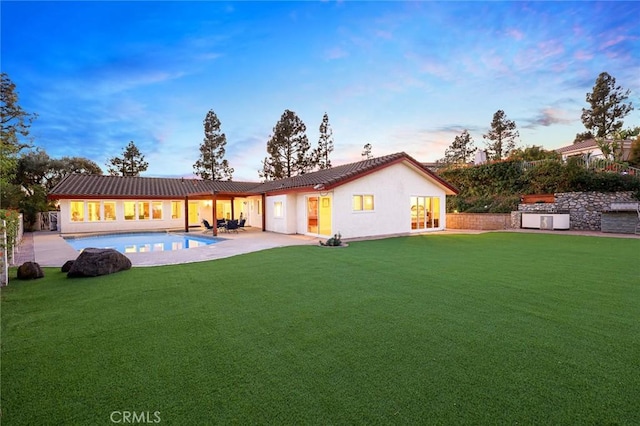 back of property at dusk with a patio area, a lawn, an outdoor pool, and stucco siding