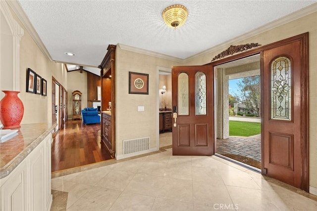 entrance foyer with visible vents, a textured ceiling, light tile patterned flooring, crown molding, and baseboards